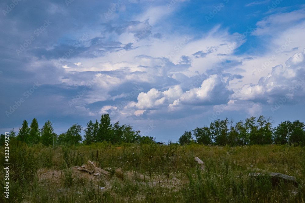 Beautiful sky and white cumulus clouds on it over trees and a field with green grass Beautiful sky and white cumulus clouds on it over trees and a field with green grass