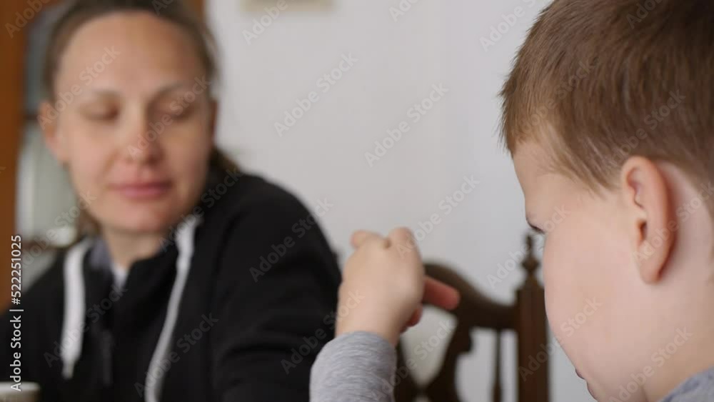 Young family drinking coffee at home. Close-up of child gesturing. Father, mom and little kid boy eat wholemeal cookies talking at wooden table. Young family drinking coffee at home. Close-up of child gesturing. Father, mom and little kid boy eat wholemeal cookies talking at wooden table.