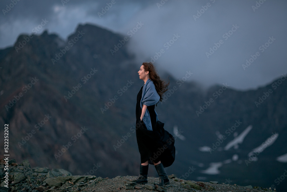 High up in the mountains. Walk in the clouds. Meet the sunset at the top of the mountain. A girl in a black dress walks on top of a mountain. North-Chuysky ridge. Wind in the hair. Freedom.