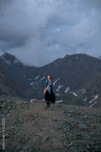 High up in the mountains. Walk in the clouds. Meet the sunset at the top of the mountain. A girl in a black dress walks on top of a mountain. North-Chuysky ridge. Wind in the hair. Freedom.