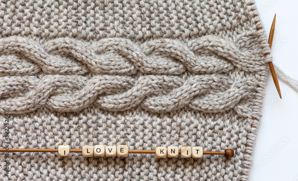 Craft and DIY concept. Wooden beads with letters with text I love to knit are strung on knitting needle and lie on handmade woolen scarf with braids. Knitted texture. Flat lay, closeup, top view Craft and DIY concept. Wooden beads with letters with text I love to knit are strung on knitting needle and lie on handmade woolen scarf with braids. Knitted texture. Flat lay, closeup, top view
