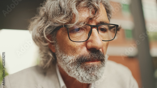 Clouse up, mature businessman with beard in eyeglasses,wearing gray jacket working using laptop pc computer sit at cafe outdoor