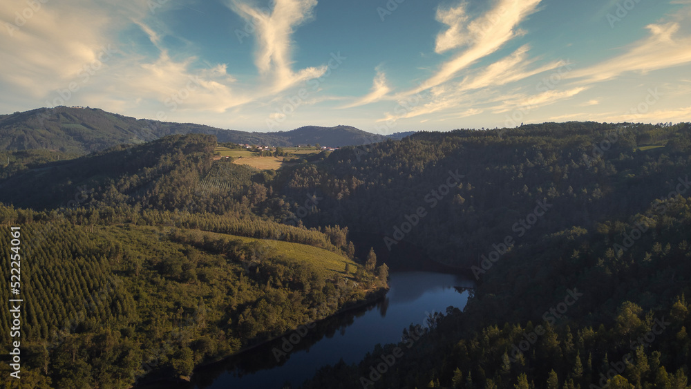 Aerial view of the river Ulla crossing a valley covered by lush forests, as it passes through the province of La Coruña, describing a beautiful meander, at sunset. 