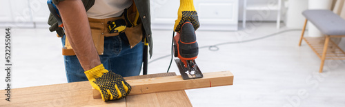 Photos Cropped view of carpenter in tool belt sawing wooden plank at home, banner