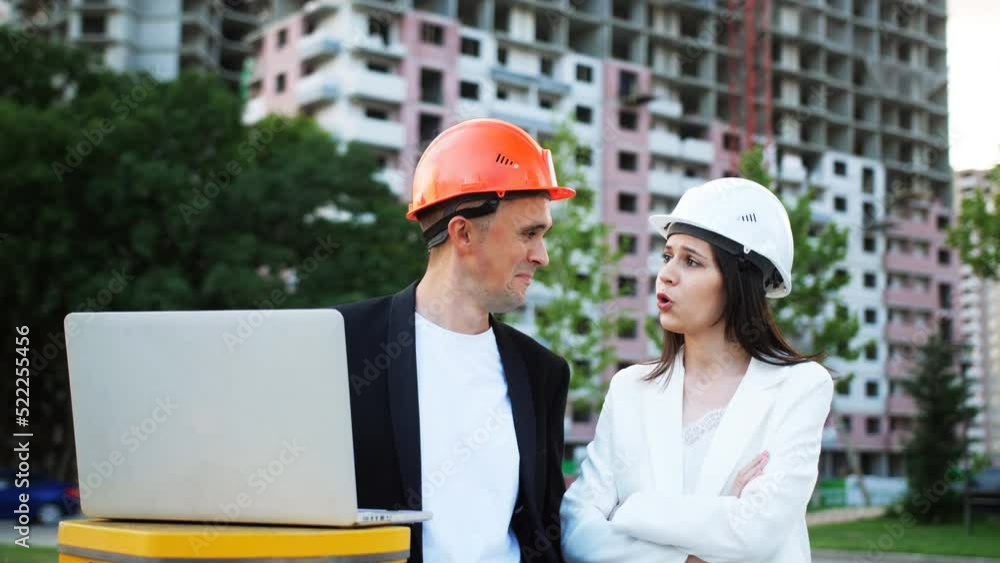 A female representative of the customer inspects the progress of construction at the facility talking to a male foreman in a construction helmet in front of a laptop. A female representative of the customer inspects the progress of construction at the facility talking to a male foreman in a construction helmet in front of a laptop.