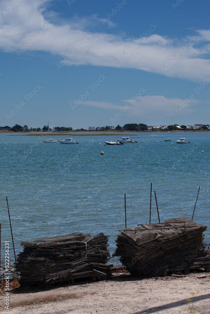 Boats at anchor in good weather. Motorboats are moored in a calm inlet. The sky is blue the weather is fine with wind. Bags of oysters are piled up in the foreground.