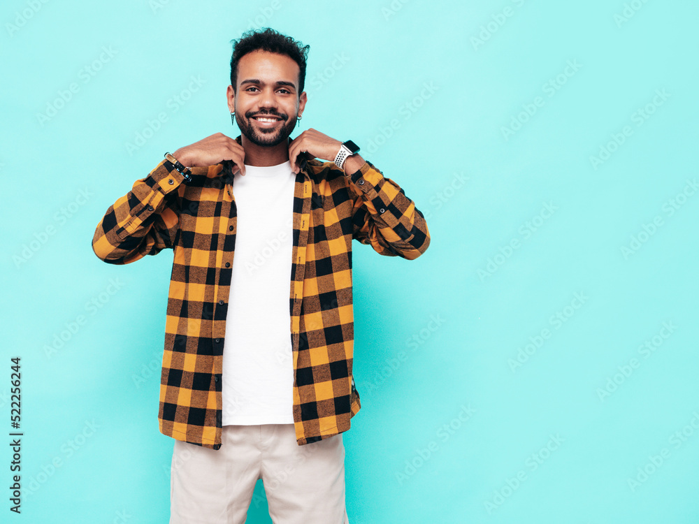 Handsome smiling hipster model. Sexy unshaven man dressed in yellow summer shirt and jeans clothes. Fashion male posing near blue wall in studio. Cheerful and happy. Isolated Handsome smiling hipster model. Sexy unshaven man dressed in yellow summer shirt and jeans clothes. Fashion male posing near blue wall in studio. Cheerful and happy. Isolated