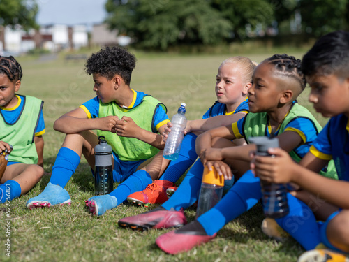 Children (8-9) dressed in uniforms sitting on soccer field