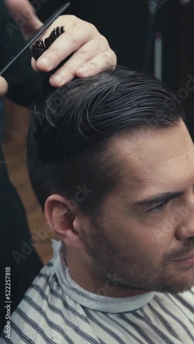 vertical video of barber cutting hair of brunette man