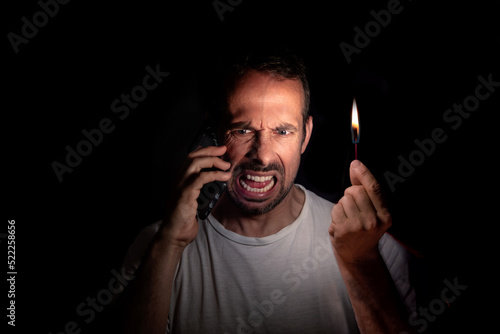 Angry man talking on the phone with a match in the dark. Blackout concept. Selective focus.