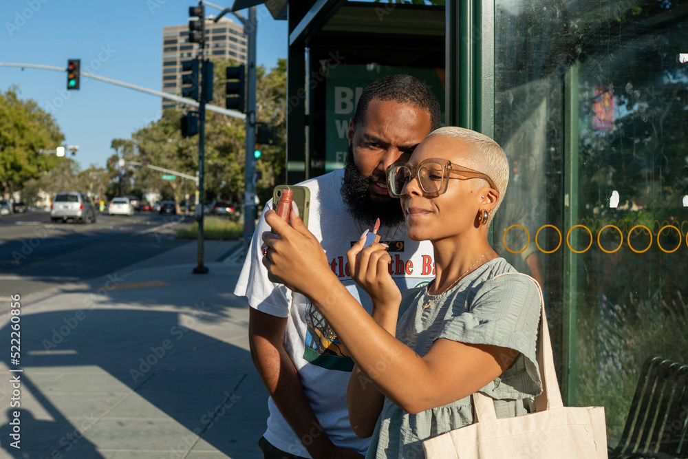 Naklejka premium Couple waiting at bus stop and woman applying lip gloss