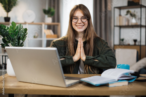 Smiling caucasian woman in casual wear sitting on workplace on yoga pose relaxing during break after working with modern laptop. Pretty female freelance meditating with open eyes.