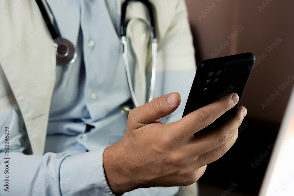 Close-up of doctor using phone at his office, doctor working online, Online consultation. Unrecognizable doctor uses smartphone at workplace, chats with patient, prescribes treatment Close-up of doctor using phone at his office, doctor working online, Online consultation. Unrecognizable doctor uses smartphone at workplace, chats with patient, prescribes treatment