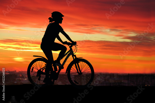 Sports, cycling, silhouette of a girl with a sports figure on a bicycle against the background of a colorful bright sunset and the city. Summer landscape, man and nature, transport. Healthy lifestyle,