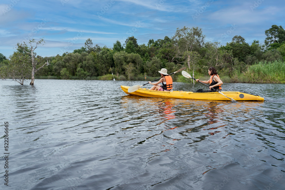 Two young Asian tourists go kayaking in a canal through the forest to see natural resources and exercise. Two young Asian tourists go kayaking in a canal through the forest to see natural resources and exercise.
