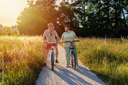 Happy smiling senior couple riding bicycles together outdoors in countryside at warm sunny day.