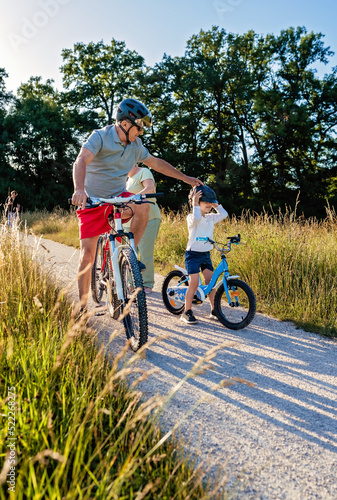 Little happy toddler boy learning how to ride bicycles with grandfather outdoors at sunny summer day.