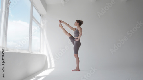 Young woman meditating near window. Girl doing exercises, practicing yoga in class. Training, workout, fitness, meditation, yoga practice, relaxation at home, healthy lifestyle concept