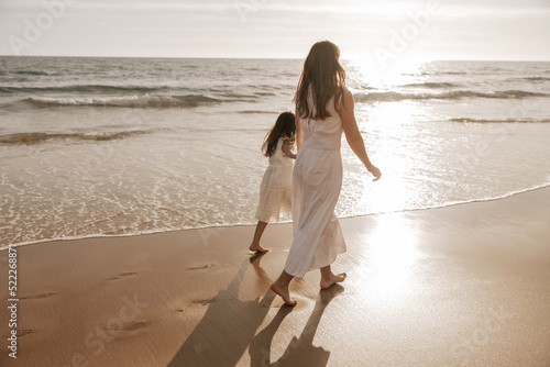 Mother and daughter walking near sea at sunrise