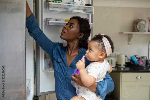 Woman looking in fridge and taking care of baby daughter (12-17 months) photo