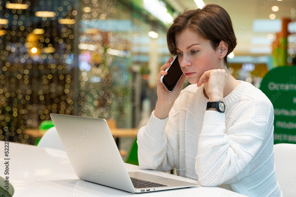 young woman talking on phone while looking at laptop young woman talking on phone while looking at laptop