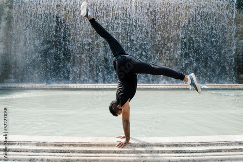 Young latin guy doing the vertical in front of a fountain in Barcelona on a sunny day. Showing strength and determination.