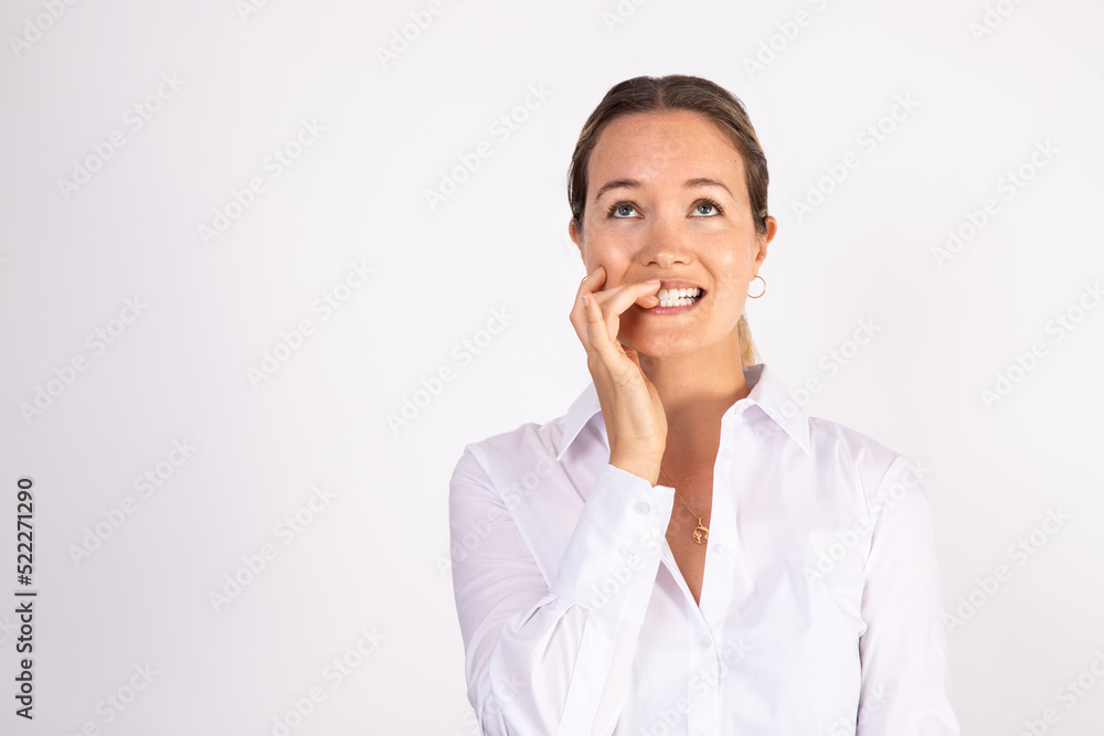 Portrait of young worried businesswoman biting nails. Depressed Caucasian woman wearing white shirt standing against white background. Fear and anxiety concept