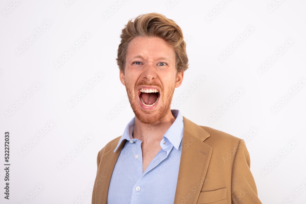 Portrait of irritated young businessman shouting with anger. Caucasian man wearing blue shirt and beige woolen suit coat crying of frustration. Businessman in trouble concept
