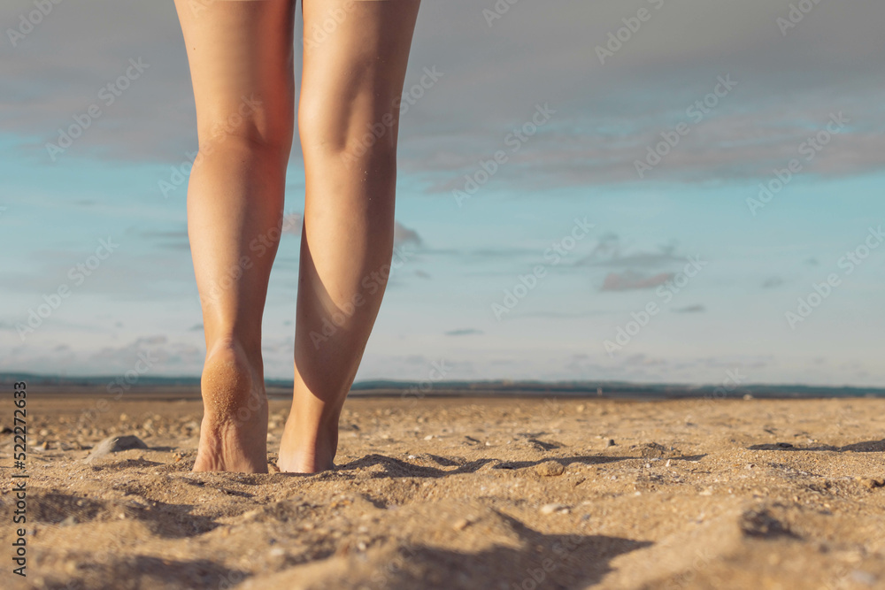 female legs against the background of the sky and sand on the beach. Female legs against the background of a sunset. Beautiful landscape, with a place for an inscription on the right side female legs against the background of the sky and sand on the beach. Female legs against the background of a sunset. Beautiful landscape, with a place for an inscription on the right side