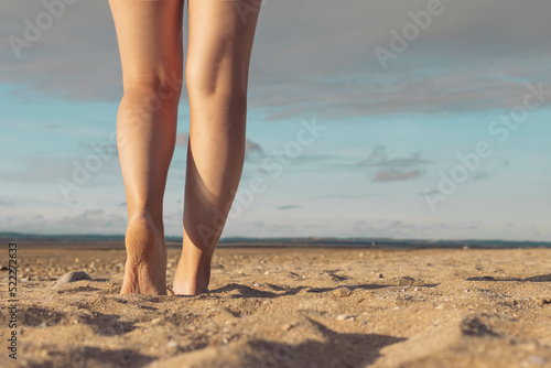 female legs against the background of the sky and sand on the beach. Female legs against the background of a sunset. Beautiful landscape, with a place for an inscription on the right side