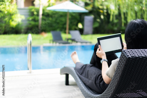 Female tourist sits on a chair by the pool at the hotel, holding a tablet with isolated screen.