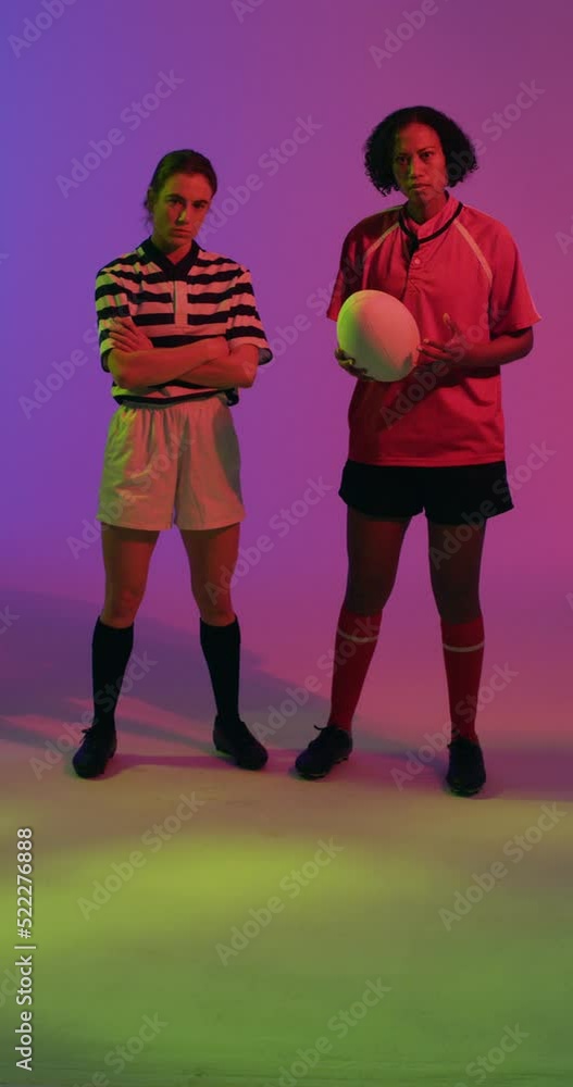 Vertical video of portrait of diverse female rugby players with rugby ball over neon pink lighting Vertical video of portrait of diverse female rugby players with rugby ball over neon pink lighting
