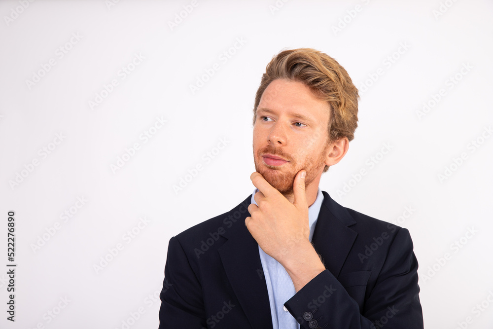 Portrait of young businessman with pensive expression. Caucasian manager wearing blue shirt and black suit coat standing and thinking with hand on chin. Business issues concept Portrait of young businessman with pensive expression. Caucasian manager wearing blue shirt and black suit coat standing and thinking with hand on chin. Business issues concept