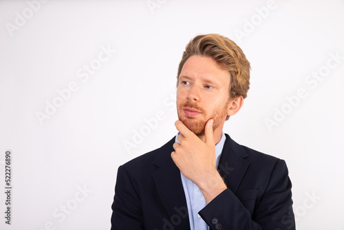 Portrait of young businessman with pensive expression. Caucasian manager wearing blue shirt and black suit coat standing and thinking with hand on chin. Business issues concept