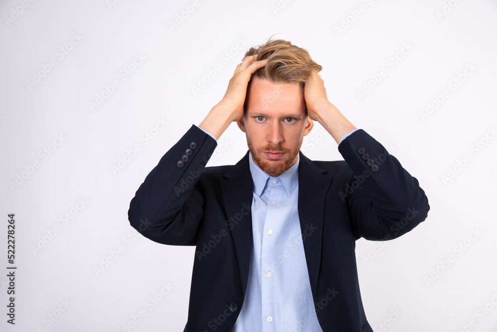 Portrait of worried young businessman clutching his head. Depressed Caucasian manager wearing blue shirt and black suit coat standing with head in hands. Problem and trouble concept Portrait of worried young businessman clutching his head. Depressed Caucasian manager wearing blue shirt and black suit coat standing with head in hands. Problem and trouble concept
