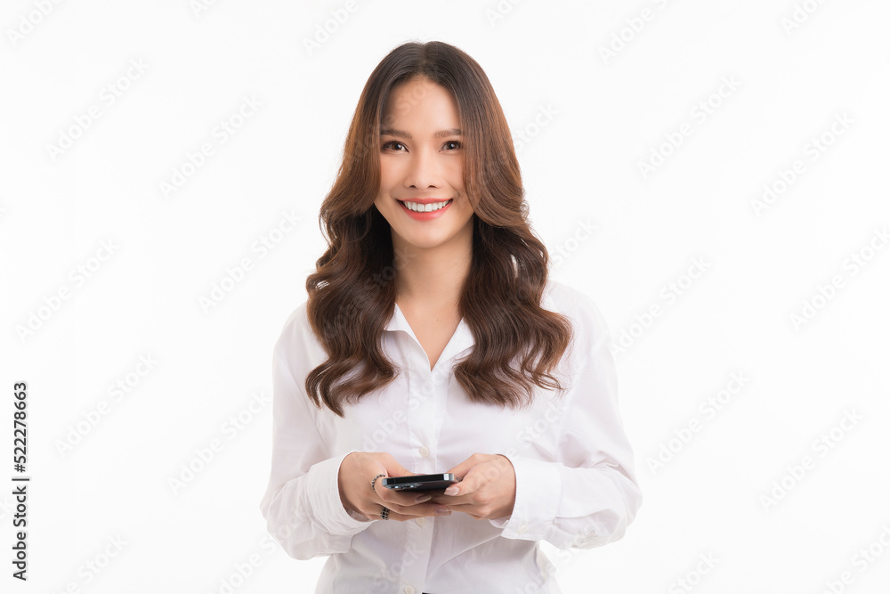 Close up photo of attractive smiling asian woman standing on white background and hold smartphone. Close up photo of attractive smiling asian woman standing on white background and hold smartphone.