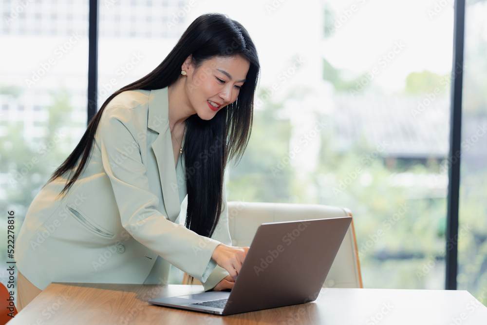 Asian young business woman sitting and smile in a office with computer laptop, Business women looking computer laptop, Business concept. Asian young business woman sitting and smile in a office with computer laptop, Business women looking computer laptop, Business concept.