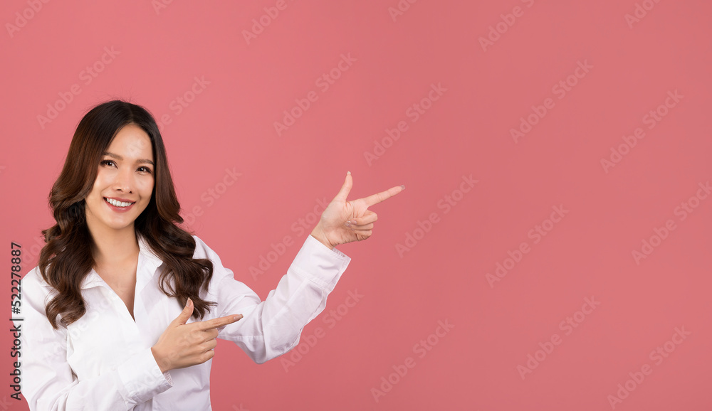 Asian woman wearing a white shirt pointing fingers at upper right corner logo banner, smiling, standing on pink background. Asian woman wearing a white shirt pointing fingers at upper right corner logo banner, smiling, standing on pink background.