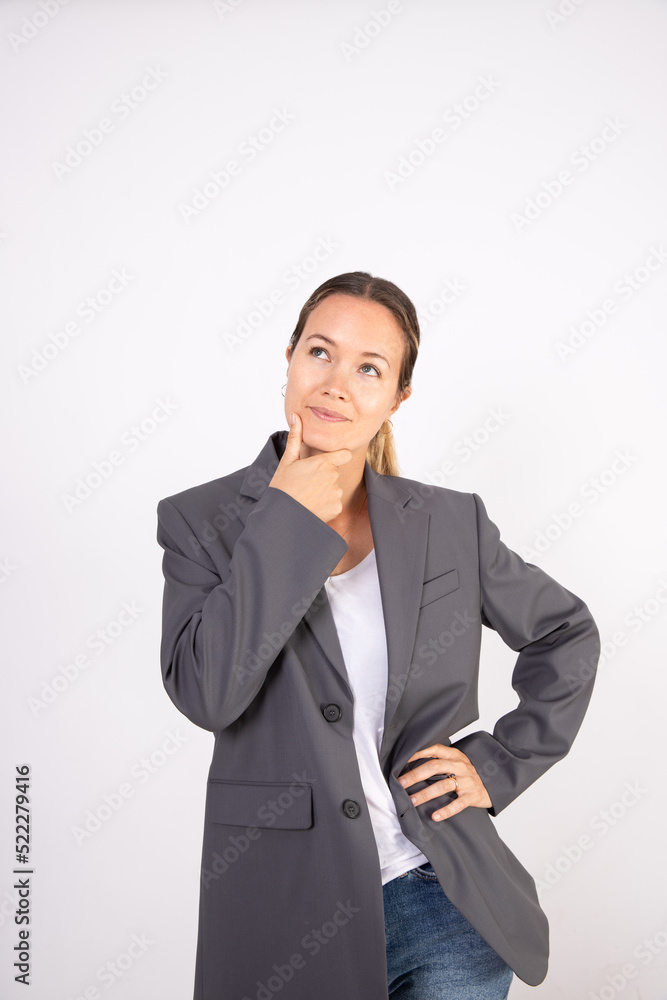 Portrait of thoughtful young businesswoman standing against white background. Caucasian woman wearing gray suit coat and white blouse having doubt or thinking. Doubt and uncertainty concept Portrait of thoughtful young businesswoman standing against white background. Caucasian woman wearing gray suit coat and white blouse having doubt or thinking. Doubt and uncertainty concept