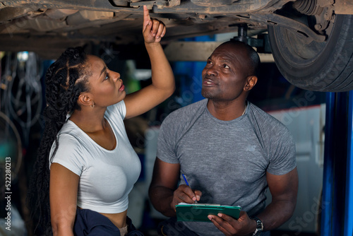 Professional Car Mechanic is Investigating Under a Vehicle on a Lift in Service. Auto Service Worker Checking Car Under Carriage Look For Issues. Car service technician check and repair customer car.