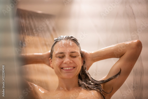 Young happy woman taking a shower washing her hair and head