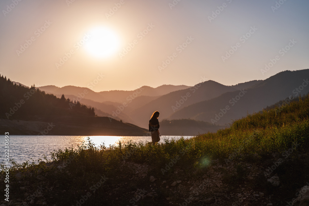 Woman traveler admiring the sunset on the shore of a lake in the mountains. Tara National Park Serbia