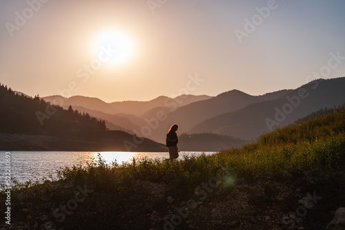 Woman traveler admiring the sunset on the shore of a lake in the mountains. Tara National Park Serbia