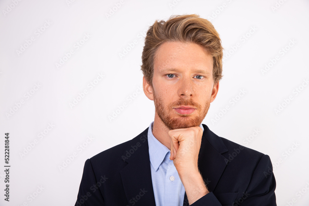 Face of concentrated businessman looking at camera. Young Caucasian manager wearing blue shirt and black suit coat standing with hand on chin. Solving problem concept Face of concentrated businessman looking at camera. Young Caucasian manager wearing blue shirt and black suit coat standing with hand on chin. Solving problem concept