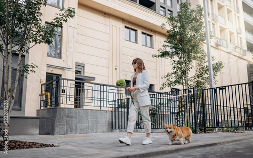 Beautiful Woman wearing white suit and sunglasses walking down the street with Welsh Corgi Pembroke dog