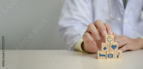 Doctor putting and stacking wooden block cube icon symbol medical health care on table panorama background concept.