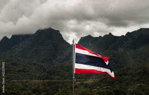 An image of Thai flag with Forest and Fog Mountain in the background. Flag of thailand waving in the wind, Natural scenery, Copy space, Selective focus.