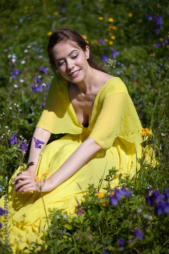 A girl in a yellow dress walks in a flowering field. The field blooms in the mountains A girl in a yellow dress walks in a flowering field. The field blooms in the mountains