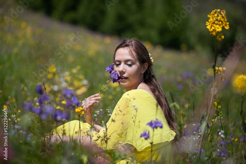 A girl in a yellow dress walks in a flowering field. The field blooms in the mountains