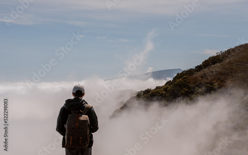Young man with a tourist backpack watching a scenic landscape of mountains and clouds, hiking in Madeira